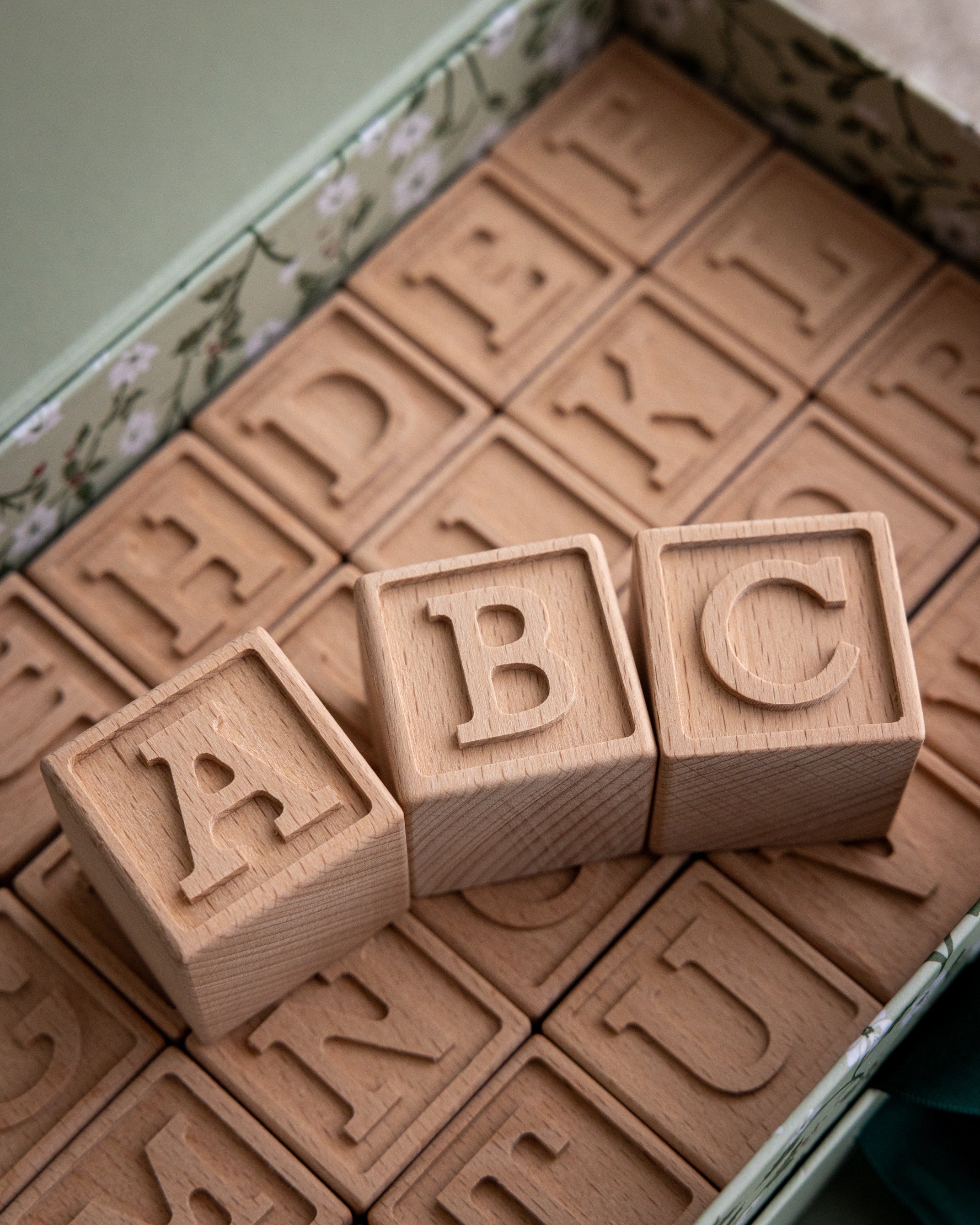 Bokstavsklossar i trä med bokstäver placerade bredvid varandra och placerade i en presentask
